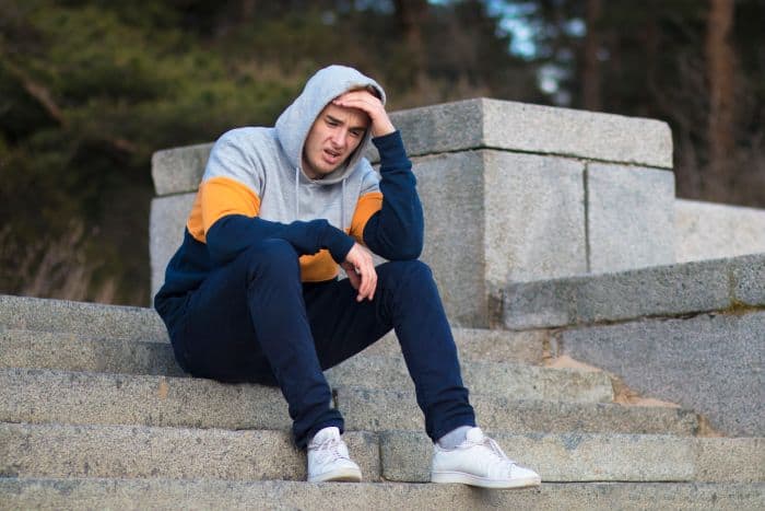 Sad man crying while sitting on steps in a hoodie