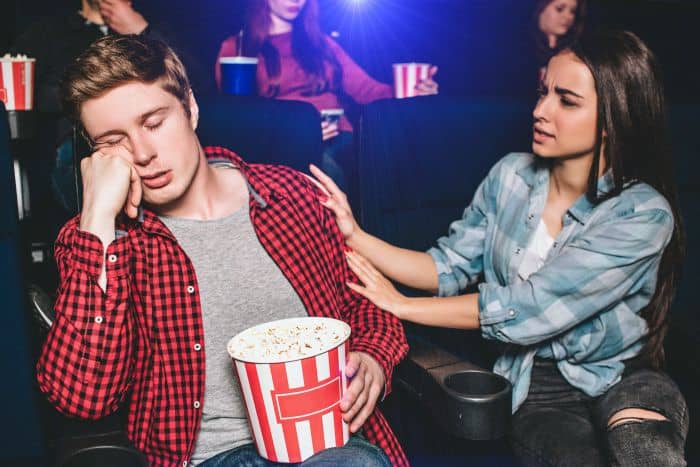Woman waking up his sleeping boyfriend in a movie theatre