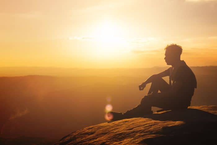Man sitting on a hilltop at sunset and thinking